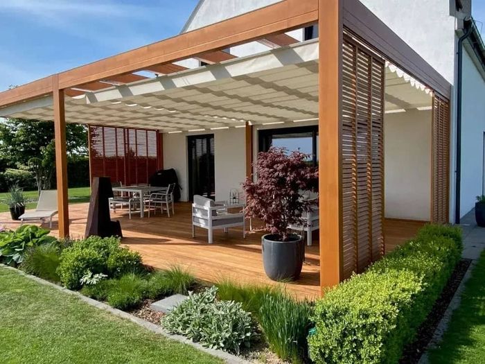 Terrasse mit Holzpergola und weißem Sonnensegel, Gartenmöbel und Topfpflanze vor modernem Haus(1)