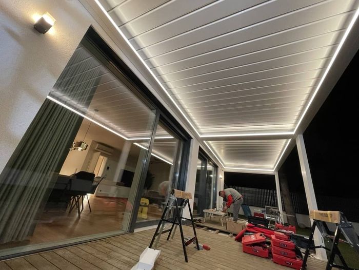 Person arbeitet nachts an einer überdachten Terrasse mit LED-Beleuchtung und Werkzeugkisten