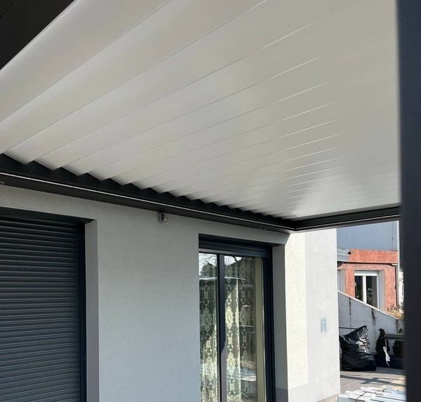 Überdachte Terrasse mit weißer Lamellendecke und Fenster mit Gardinen an einem modernen Haus