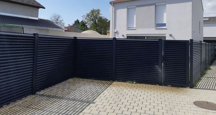 Einfriedung mit schwarzem Sichtschutzzaun aus Metall vor einem weißen Wohnhaus mit zwei Fenstern