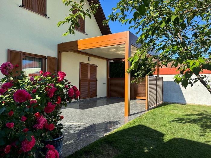 Eine friedliche Szene im Hinterhof mit einem modernen Haus, braunen Fensterläden und einer Holzpergola auf einer gefliesten Terrasse. Lebhafte rosa Rosen und ein grüner Rasen verleihen dem Ganzen zusätzlichen Charme.