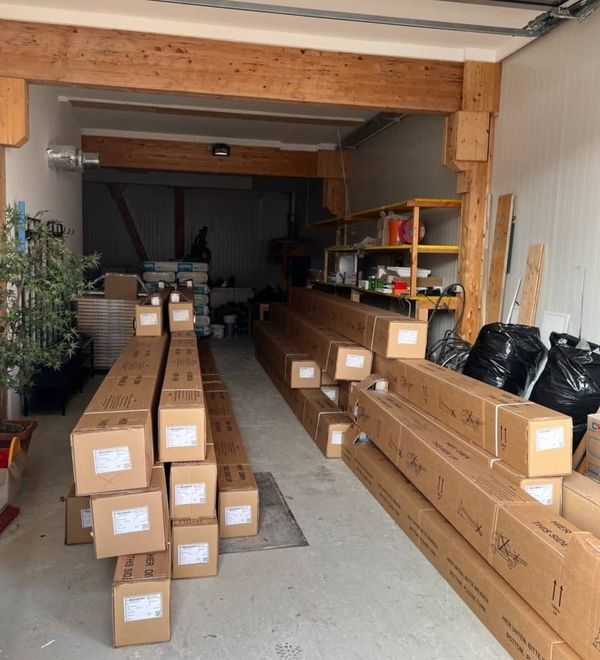 Lagerraum mit gestapelten langen Kartons und Regalen mit weiteren Kartons und Gegenständen