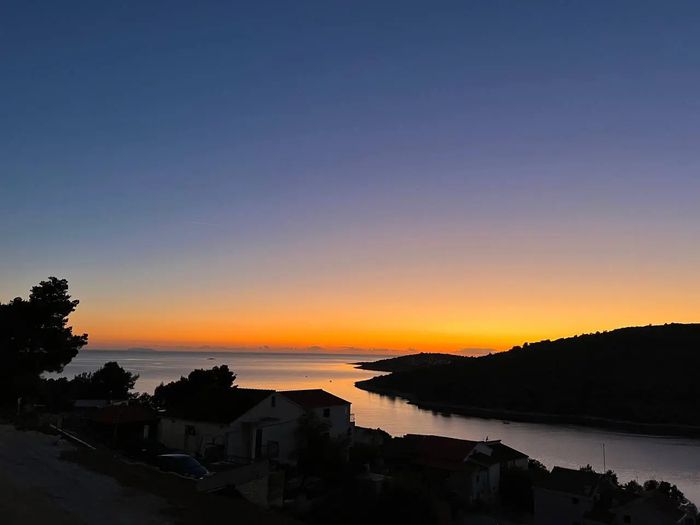 Sonnenuntergang über ruhiger Bucht mit Silhouetten von Häusern und Bäumen am Ufer