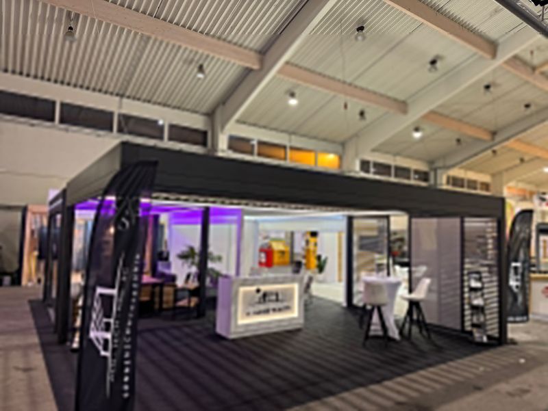 Moderner Messestand mit eleganter Beleuchtung in Schwarz und Violett. Mit Sitzgelegenheiten, einer weißen Rezeption und Markenflaggen. Professionelle und einladende Atmosphäre.