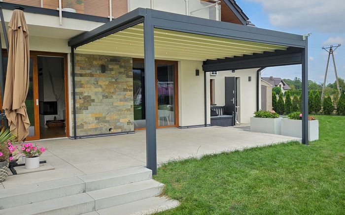 Moderner Wintergarten mit grauem Aluminiumrahmen und verstellbarem Lamellendach an einem Haus mit Terrasse und Garten